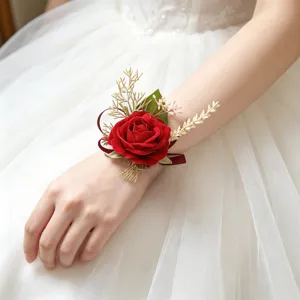 Detailed view of elegant red artificial rose wrist flower with green leaves for wedding decor.