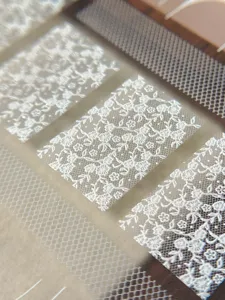 Close-up detail of vintage white lace floral nail stickers for DIY manicure designs.