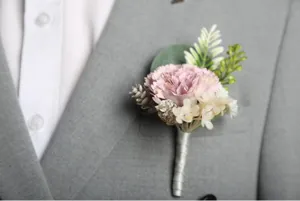 Close-up detail of artificial wedding boutonniere corsage with pink flower and white ribbon.