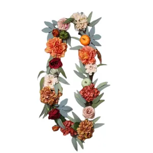 Autumn artificial floral wreath featuring cute pumpkins and green leaves for home decoration.