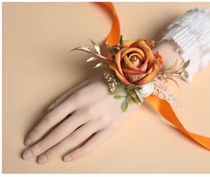 Close-up detail van de elegante oranje roos polscorsage met gouden bladeren en een lint.