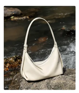 Detailed shot of a stylish off-white leather hobo bag resting on a natural stream rock.
