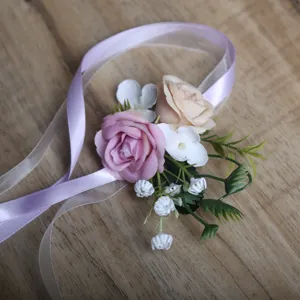 Close-up detail of artificial rose wrist corsage with purple and champagne flowers and ribbons.
