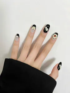Primer plano detallado de uñas postizas en blanco y negro con flores 3D y lazos decorativos.