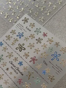 Close-up of 3D metallic flower nail stickers featuring embossed details and text.