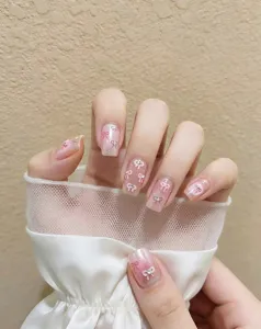 Primer plano detallado de uñas postizas con bonitos lazos rosados y brillantes pedrería.