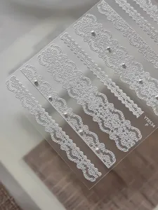 Detailed close-up of white lace embossed nail stickers featuring elegant pearl and ribbon designs.