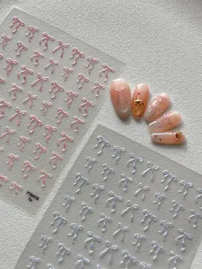 Detalle de pegatinas de uñas con lazo iridiscente 3D con hojas rosa y azul y uñas postizas.