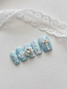 Detalle de uñas postizas azules elegantes con encaje blanco y pedrería brillante.