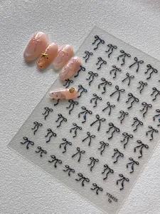 Vista detallada de pegatinas de uñas 3D con lazo iridiscente y expositor de uñas postizas.