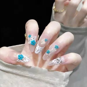 Long almond false nails featuring elegant white lace french tips and blue floral charms.