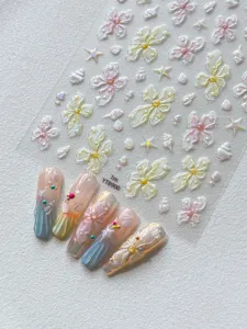 Detailed view of pearlescent flower and shell nail art stickers with 3D crystal bead designs.