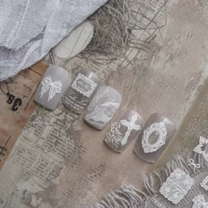 Closeup detail of retro press-on nail stickers featuring white lace, bows, and gothic crosses.