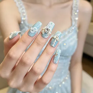 Uñas postizas azul claro elegantes con delicado encaje blanco, lazos bonitos y pedrería brillante.