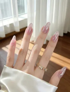 Uñas postizas largas de almendra con degradado rosa y diseño de estrellas plateadas elegantes.
