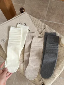 Close up of soft cotton solid color slouch socks in white, beige, and dark grey tones.