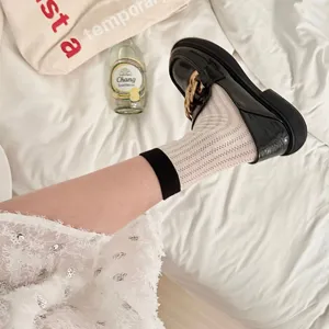 Detail shot of hollow-out mid-tube socks paired with stylish black loafers on white bedding.