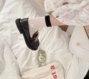 Detailed shot of hollowed-out knit socks paired with black patent leather loafers on bed.