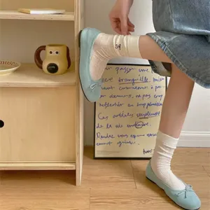 Close-up detail of white ribbed mid-tube socks with cute bow embroidery, paired with blue flats.