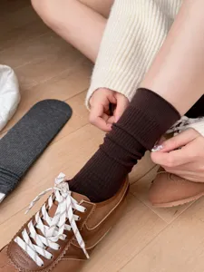 Close-up view of ribbed mid-tube socks worn with brown sneakers on wooden floor background.