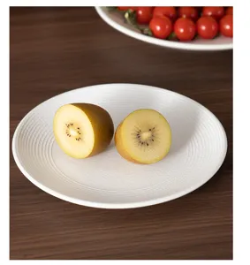 Detailed view of white ceramic plate with elegant ribbed texture holding fresh kiwi fruit.