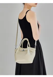 Primo piano di una chic borsa a secchiello in pelle beige con chiusura a torsione e tracolla.