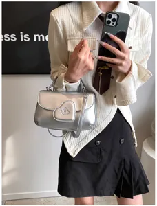 Nahaufnahme einer stylischen silbernen PU-Handtasche mit Herzklappe und Metallgriff.