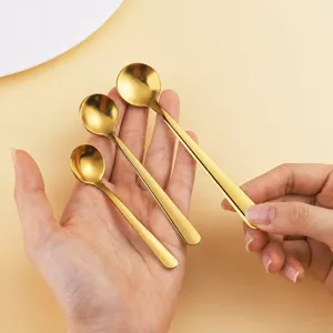 Primer plano de mini cucharas redondas doradas de acero inoxidable sujetadas en mano.