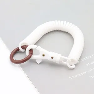 Détail de porte-clés à ressort blanc, avec un anneau rond marron et un mousqueton.
