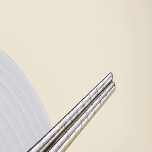 Nahaufnahme von Metall-Essstäbchen mit Anti-Rutsch-Ringen vor neutralem Beigebett.
