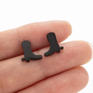 Detailed close-up shot of miniature black cowboy boot stud earrings on human fingers.