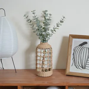 Vue détaillée d'un vase en verre enveloppé de corde en papier avec des branches d'eucalyptus.