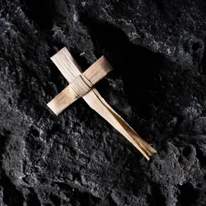 Primer plano del detalle de la cruz tejida a mano sobre roca oscura, decoracion rústica.