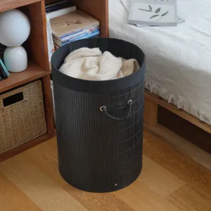Detailed view of black cylindrical bamboo woven laundry basket with rope handles in bedroom scene.