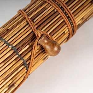 Detailed view of natural reed roll blind featuring strong brown binding cords and wooden toggle.