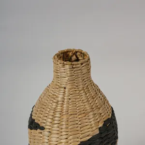 Gros plan d'un vase en paille tissé à la main avec un design bicolore naturel et noir.