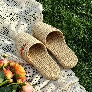 Close-up of handmade woven straw slippers with cute embroidery, rustic lifestyle grass scene.