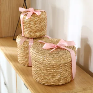 Round straw woven storage basket with lid and pink ribbon, perfect desktop organizer.