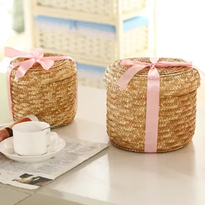 Detailed shot of woven straw storage basket with pink ribbon bow on white tabletop scene.