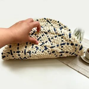 Close-up detail of hand holding woven straw placemat, showcasing natural texture and blue pattern.