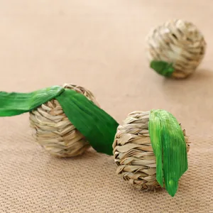 Handcrafted straw woven pet ball chew toy with green leaf, natural material detail shot.