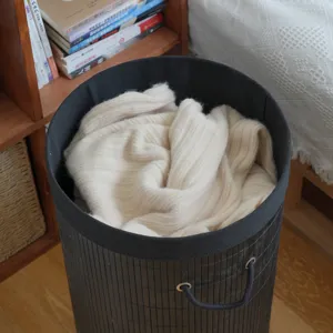 Black cylindrical bamboo laundry basket with beige knit garment, collapsible home storage hamper.