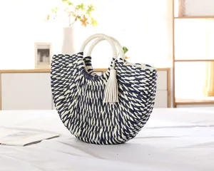 Closeup detail of woven straw half moon handbag with blue and white pattern and tassel accent.