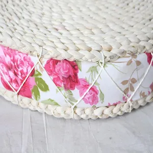 Detailed view of handmade straw woven cushion, pink floral fabric side with white rope tie.