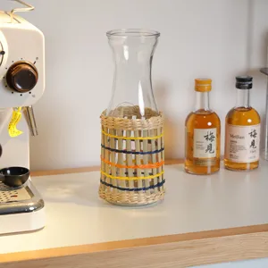 Gedetailleerd close-up van een heldere glazen fles met een handgeweven strohoes op tafel.