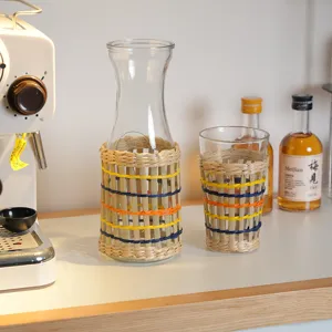 Detailopname handgemaakte glazen kan en beker met strogevlochten hoes, rustiek interieurdecor.