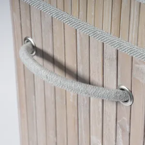 Détail de panier de rangement en bambou tressé avec poignée en tissu gris et œillets.