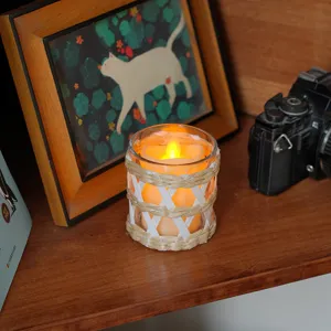 Primer plano del portavelas de vidrio y paja tejida en estante, decoración acogedora del hogar.