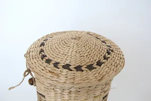 Detalle de cesta de almacenamiento tejida a mano con fibras naturales y tapa decorativa.