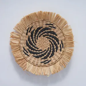 Detailed view of bohemian round straw woven wall hanging with black spiral pattern and fringe.